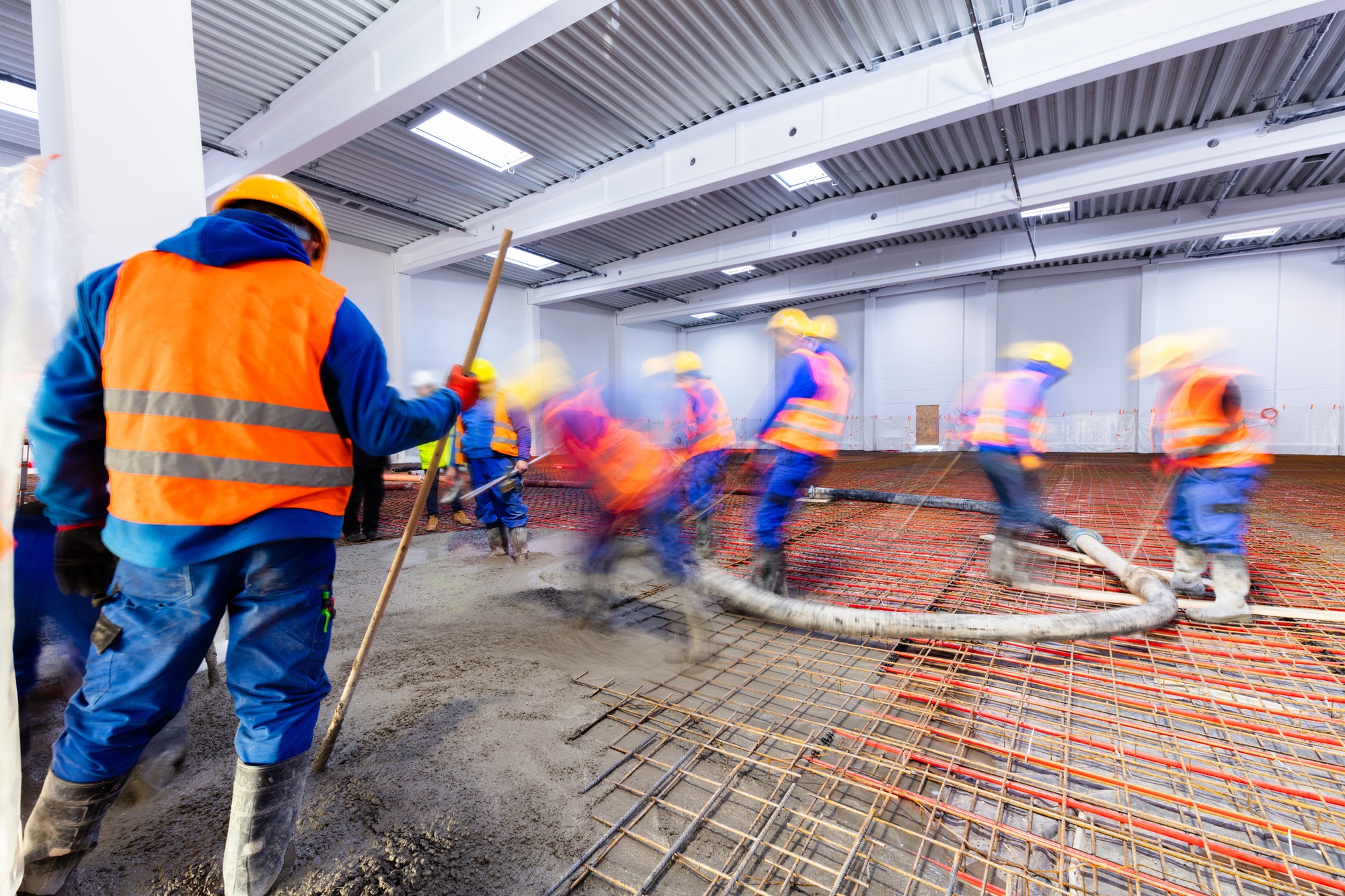 Workers do concrete screed on floor with heating in a new warehouse building